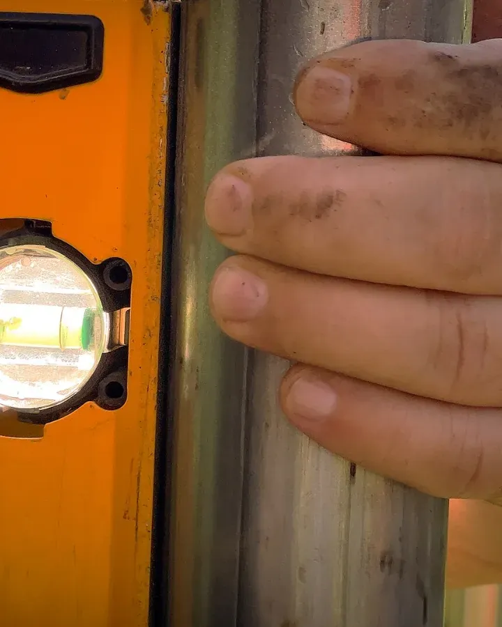 Close-up of a hand holding a level against a metal post.